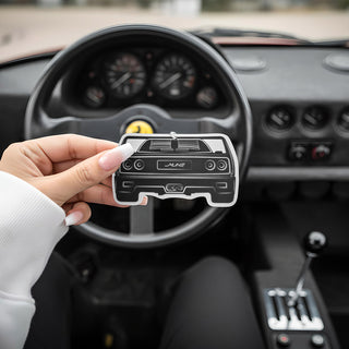 Hand holding Ferrari F40 V8 silhouette air freshener with classic analog sports car dashboard in background