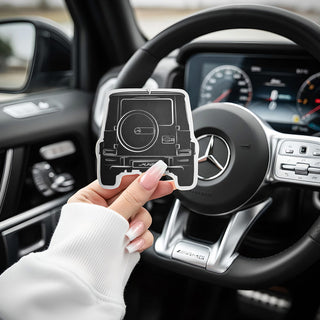 Mercedes G Wagon G63 hand holding G-Series silhouette air freshener with modern SUV dashboard and steering wheel.